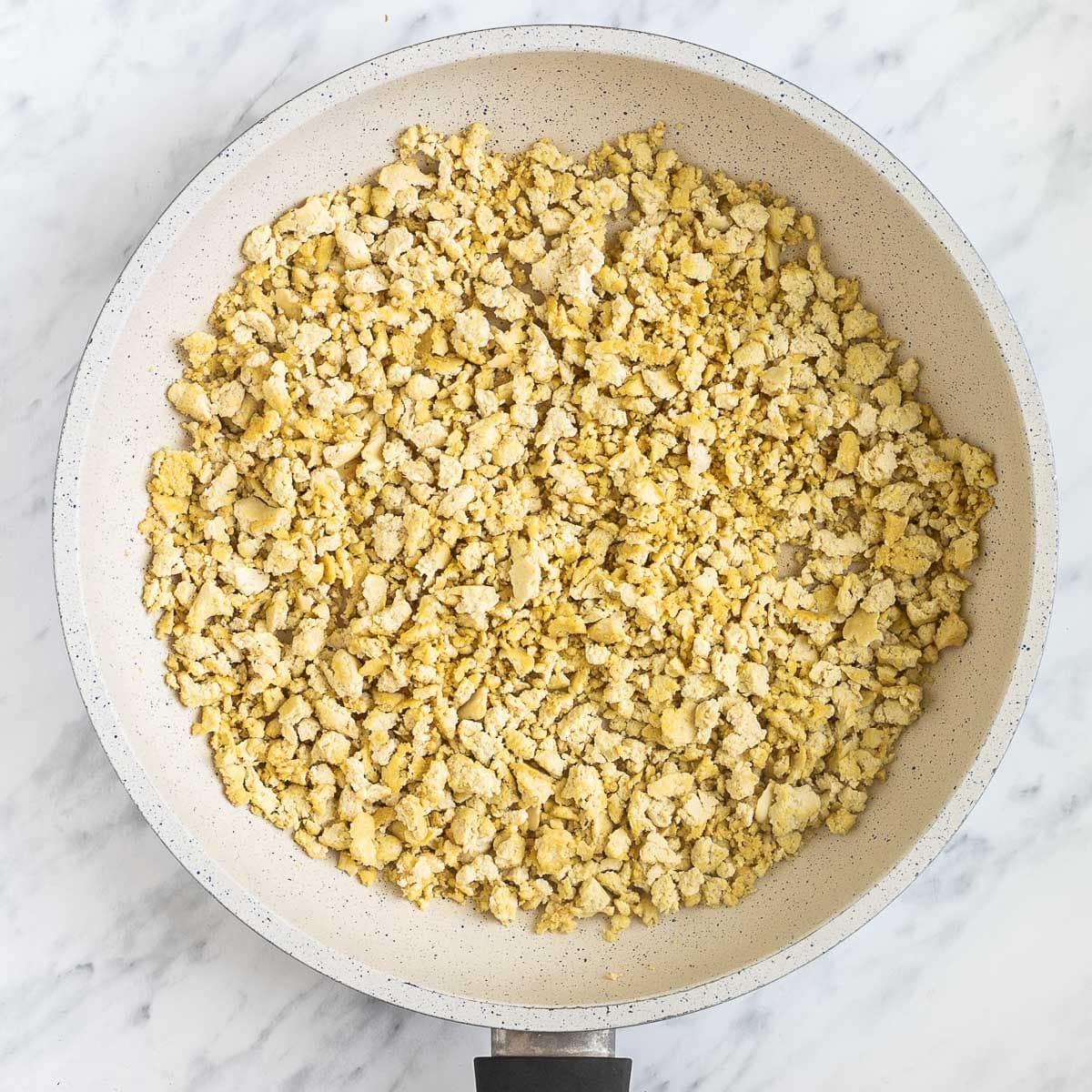 White frying pan with lightly toasted tofu crumbles.