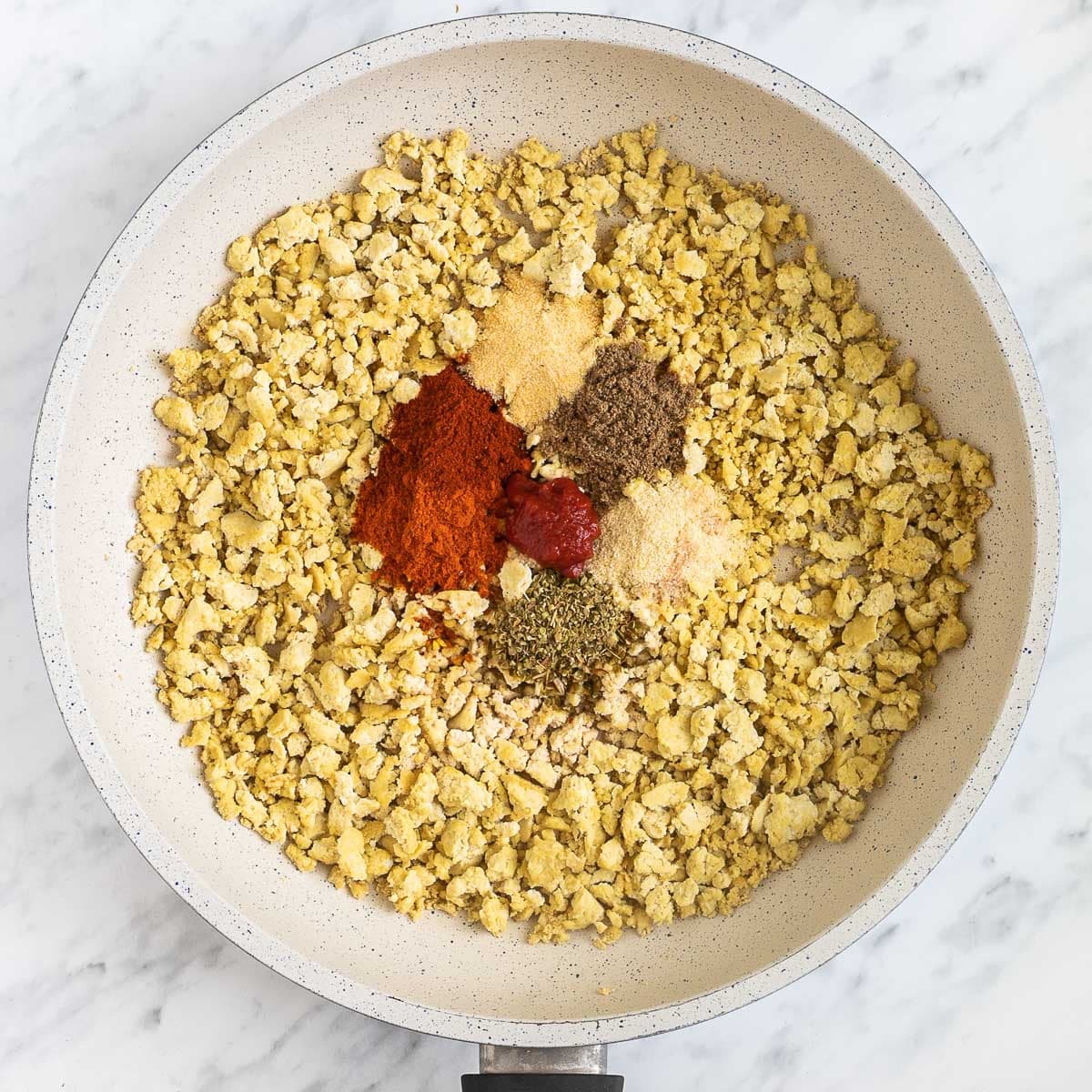 White frying pan with lightly toasted tofu crumbles and 5 different spices from red to brown.