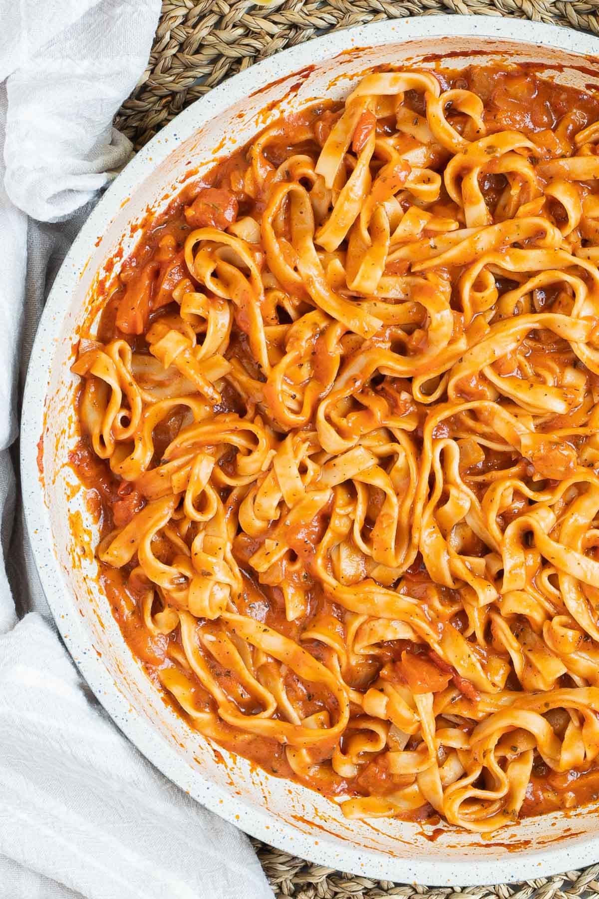 Tagliatelle is mixed in and covered with a creamy light red tomato-based sauce in a white frying pan.