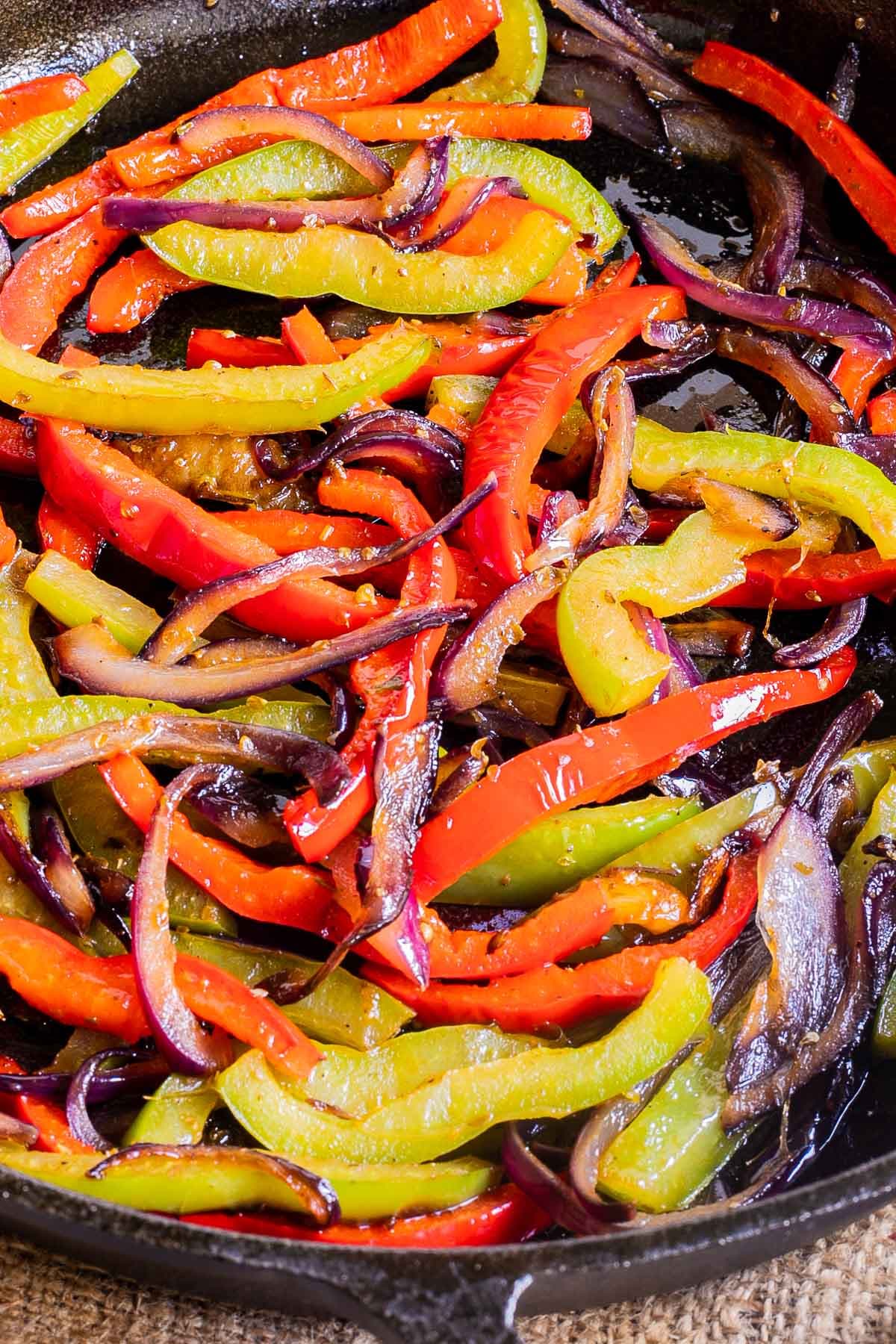 Black cast iron skillet with slightly brown red and green bell pepper strips and red onion slices.