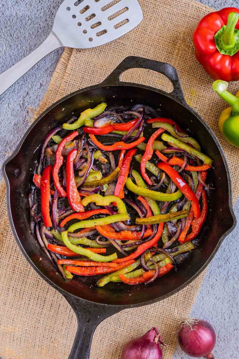 Black cast iron skillet with slightly brown red and green bell pepper strips and red onion slices.