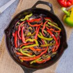 Black cast iron skillet with slightly brown red and green bell pepper strips and red onion slices.