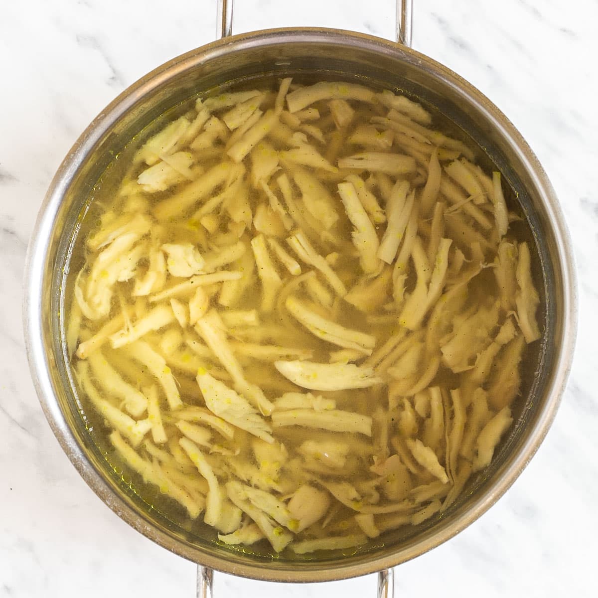 Stockpot with yellow broth and shredded mushrooms.