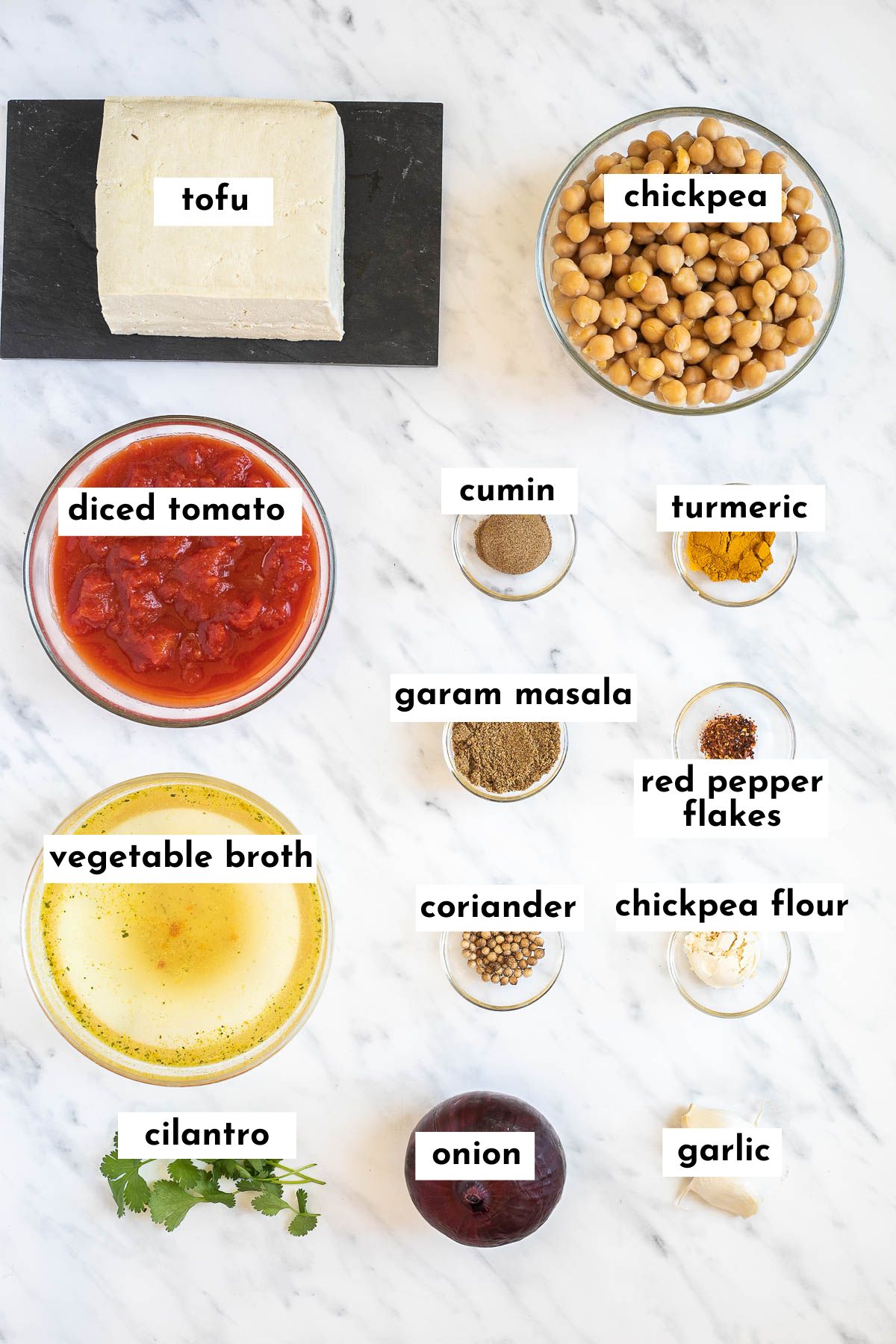 The ingredients of chickpea tofu curry is in small glass bowls like tofu, chickpeas, diced tomatoes, veggie broth, different spices and freshly chopped herbs.