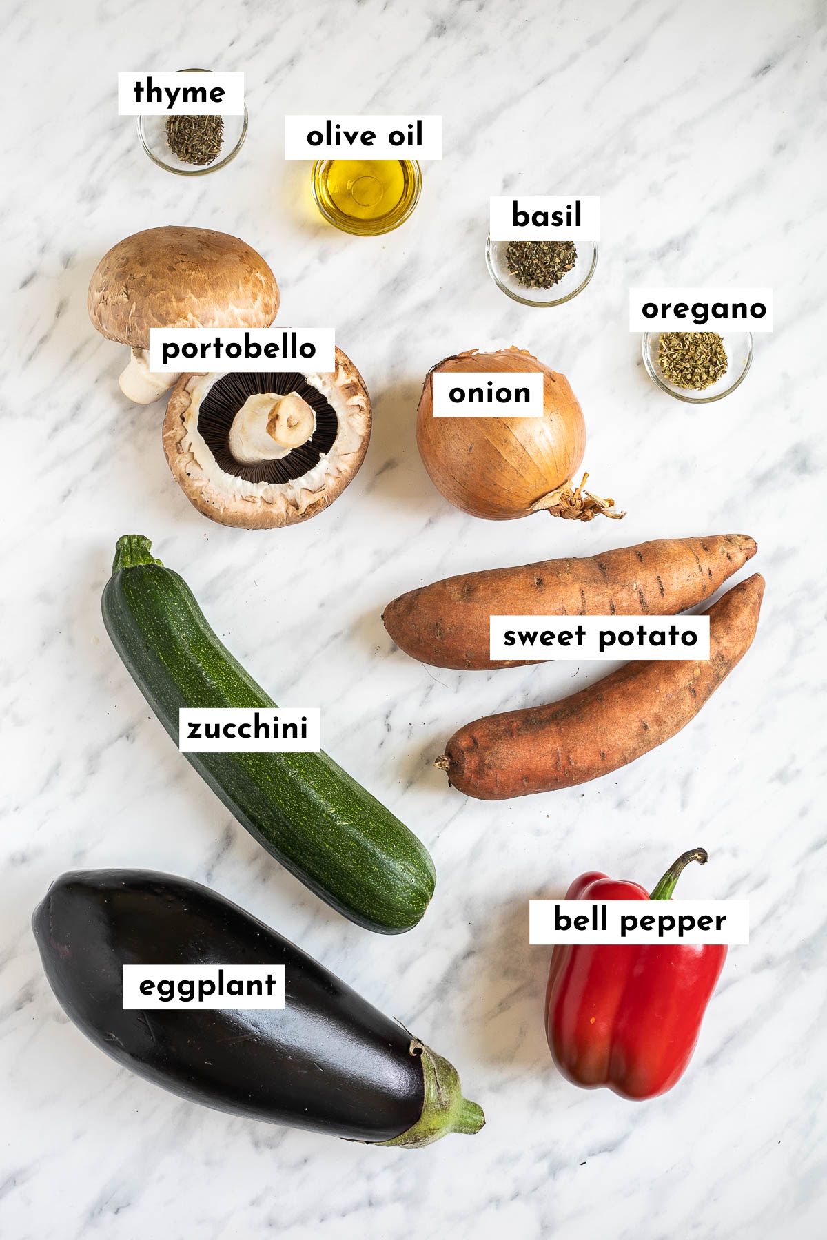 The ingredients of vegetable napoleon on a marble surface including eggplant, zucchini, sweet potato, red bell pepper, mushroom, onion and 4 spices in small glass bowls.