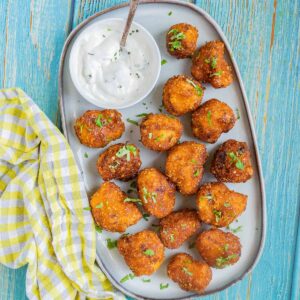 Breaded cauliflower florets in a light blue plate sprinkled with chopped green herbs and served with a small bowl of white sauce