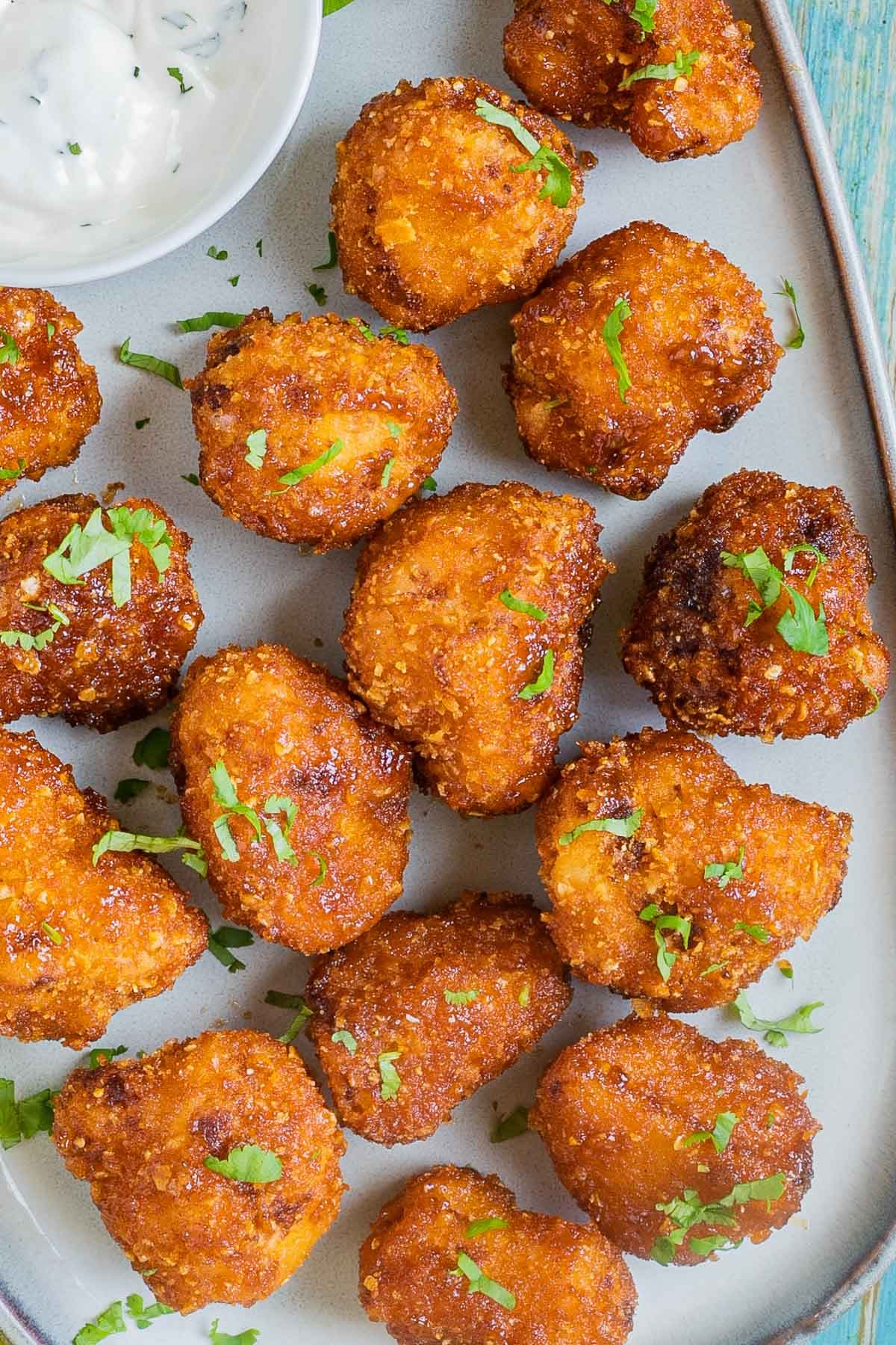 Breaded cauliflower florets in a light blue plate sprinkled with chopped green herbs and served with a small bowl of white sauce
