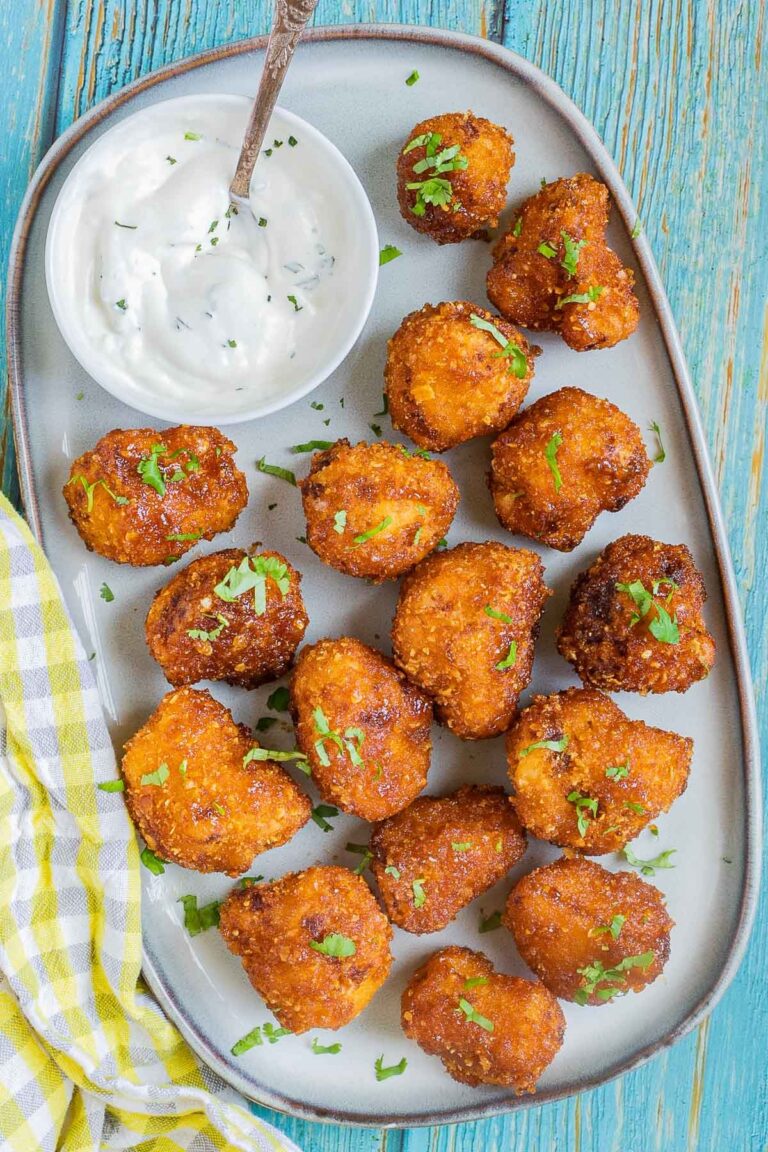 Breaded cauliflower florets in a light blue plate sprinkled with chopped green herbs and served with a small bowl of white sauce