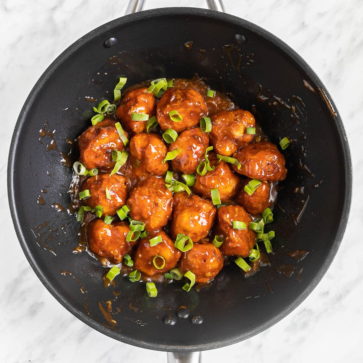 Orange sauce glazed cauliflower florets in a wok sprinkled with chopped green scallions.