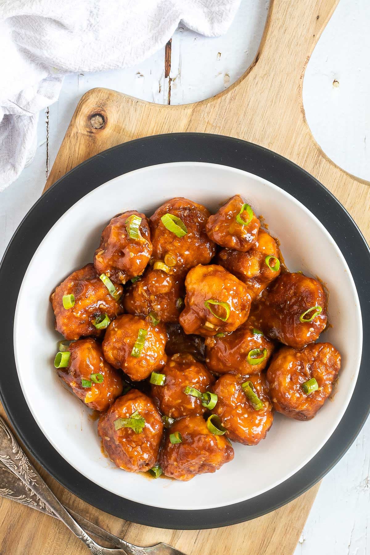 Orange sauce glazed cauliflower florets sprinkled with chopped green scallions in a white plate.