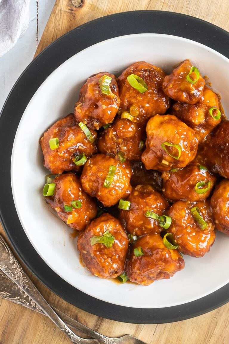 Orange sauce glazed cauliflower florets sprinkled with chopped green scallions in a white plate.