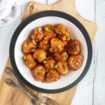 Orange sauce glazed cauliflower florets sprinkled with chopped green scallions in a white plate.