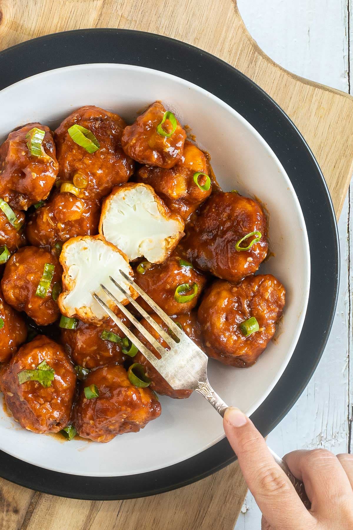 Orange sauce glazed cauliflower florets sprinkled with chopped green scallions in a white plate. One floret is cut in half so you can see the white cauliflower inside.