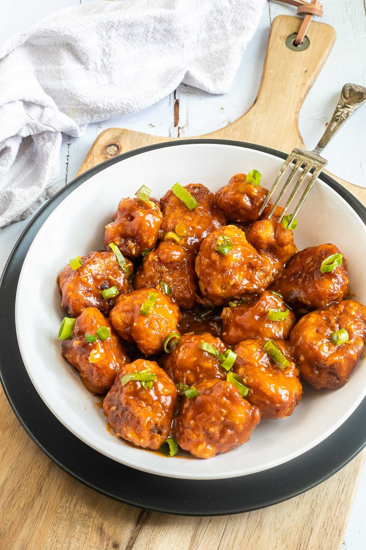 Orange sauce glazed cauliflower florets sprinkled with chopped green scallions in a white plate.