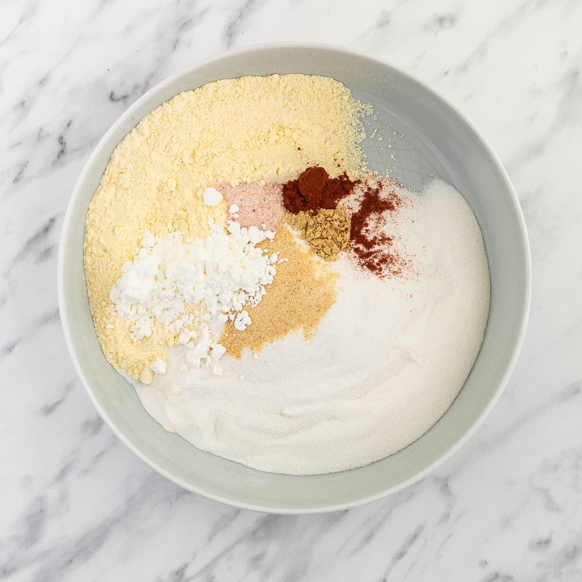 White bowl with white and yellow flour and red to yellow spices.