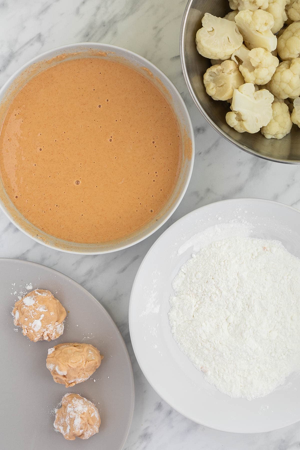 1 bowl with orange wet batter, 1 bowl with white flour, 1 bowl with cooked cauliflower florets and 1 plate with 3 battered cauliflower florets