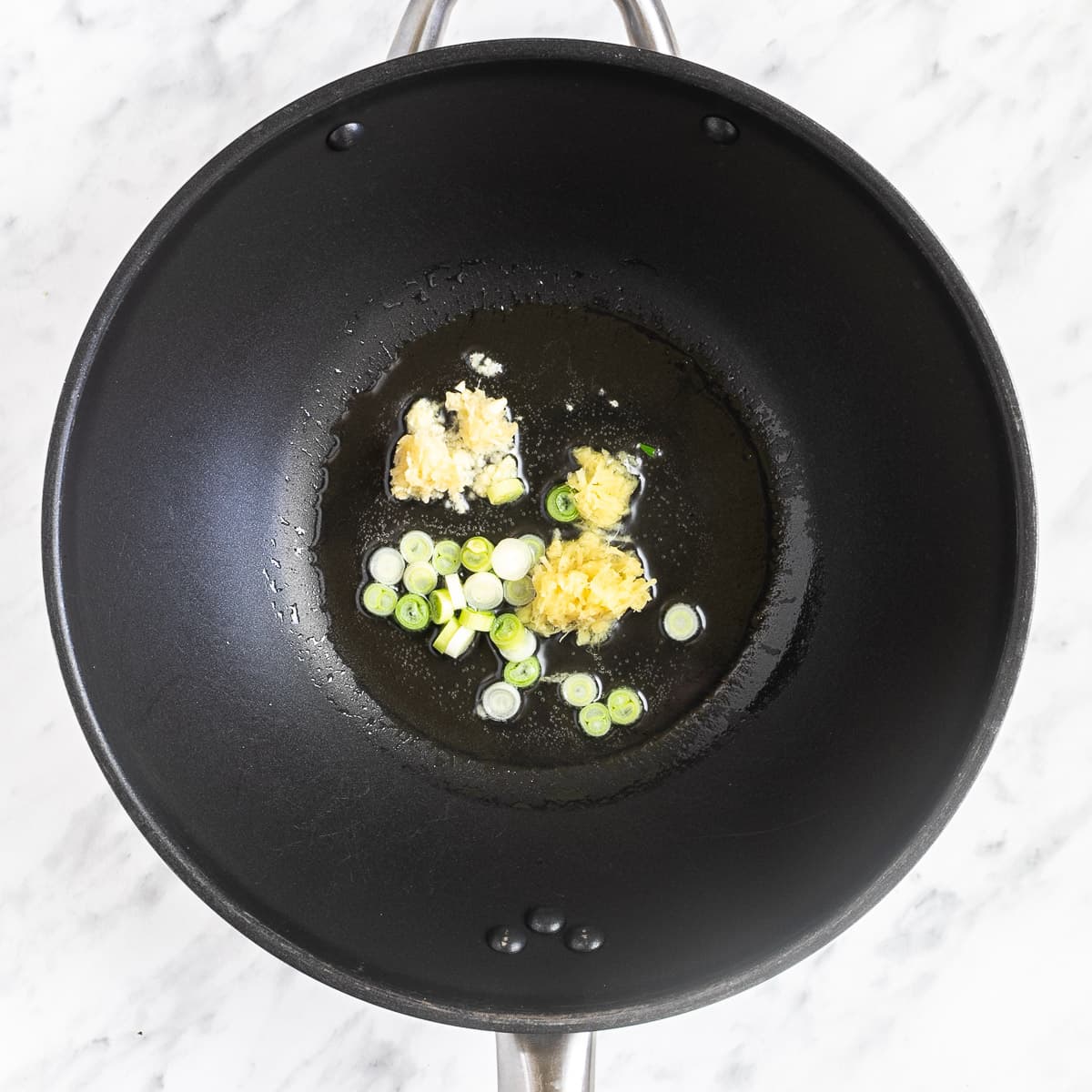 A wok with chopped onion, garlic, and ginger.