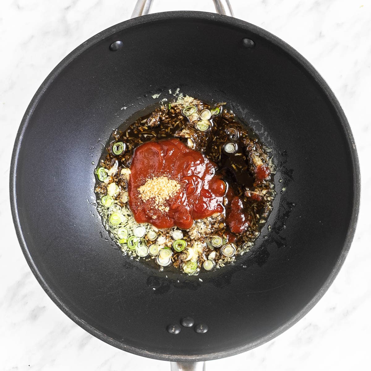 A wok with chopped onion, garlic, ginger, and red sauce.