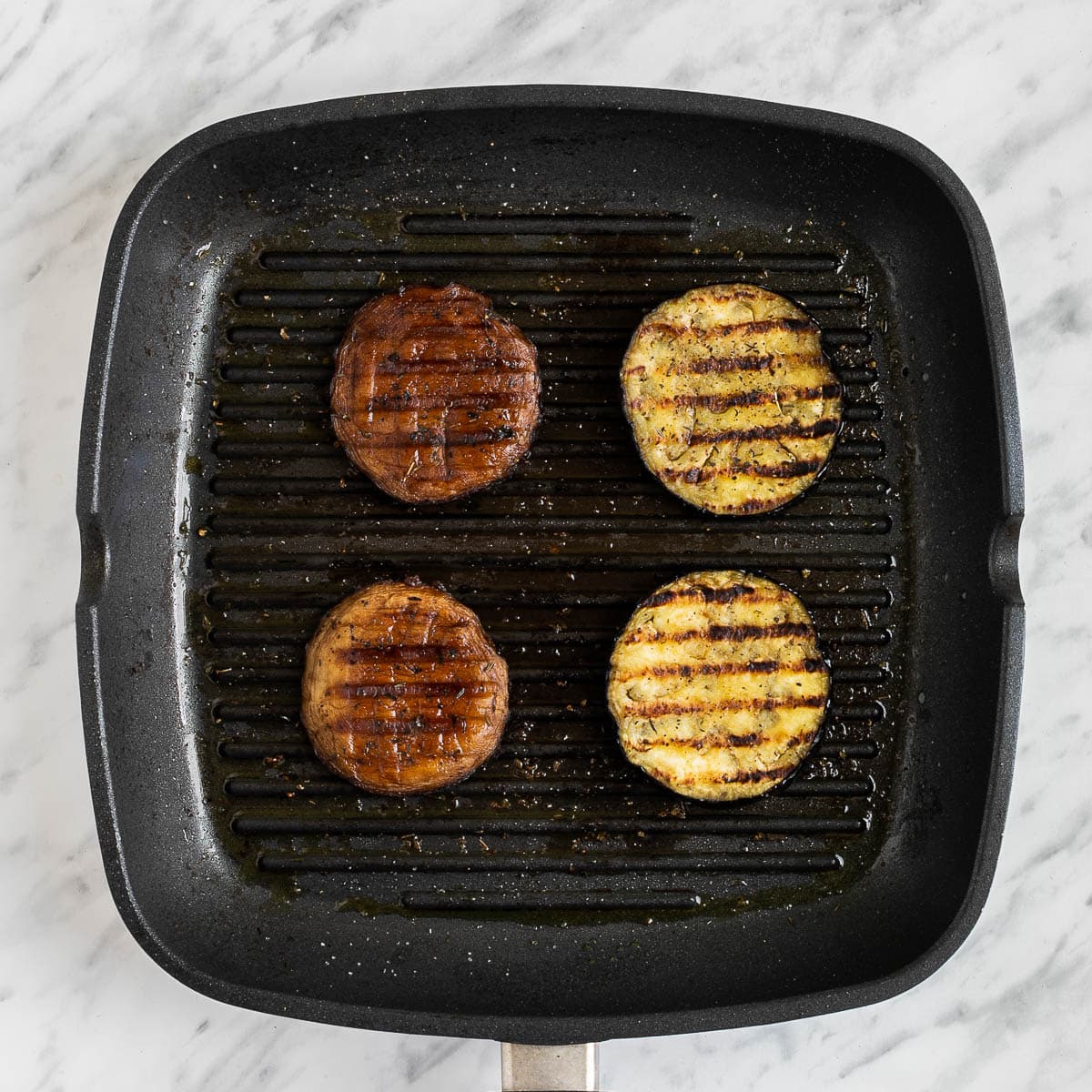 Grill pan with 2 charred portobello mushrooms caps and 2 eggplant slices.