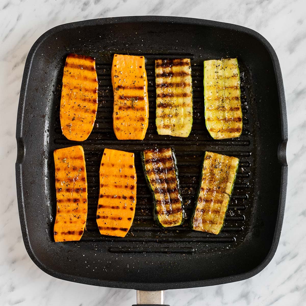 Grill pan with 2 charred sweet potato, and 2 charred zucchini slices.