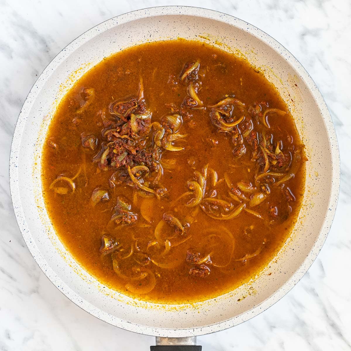 Onion slices in an orange brown sauce in a white frying pan