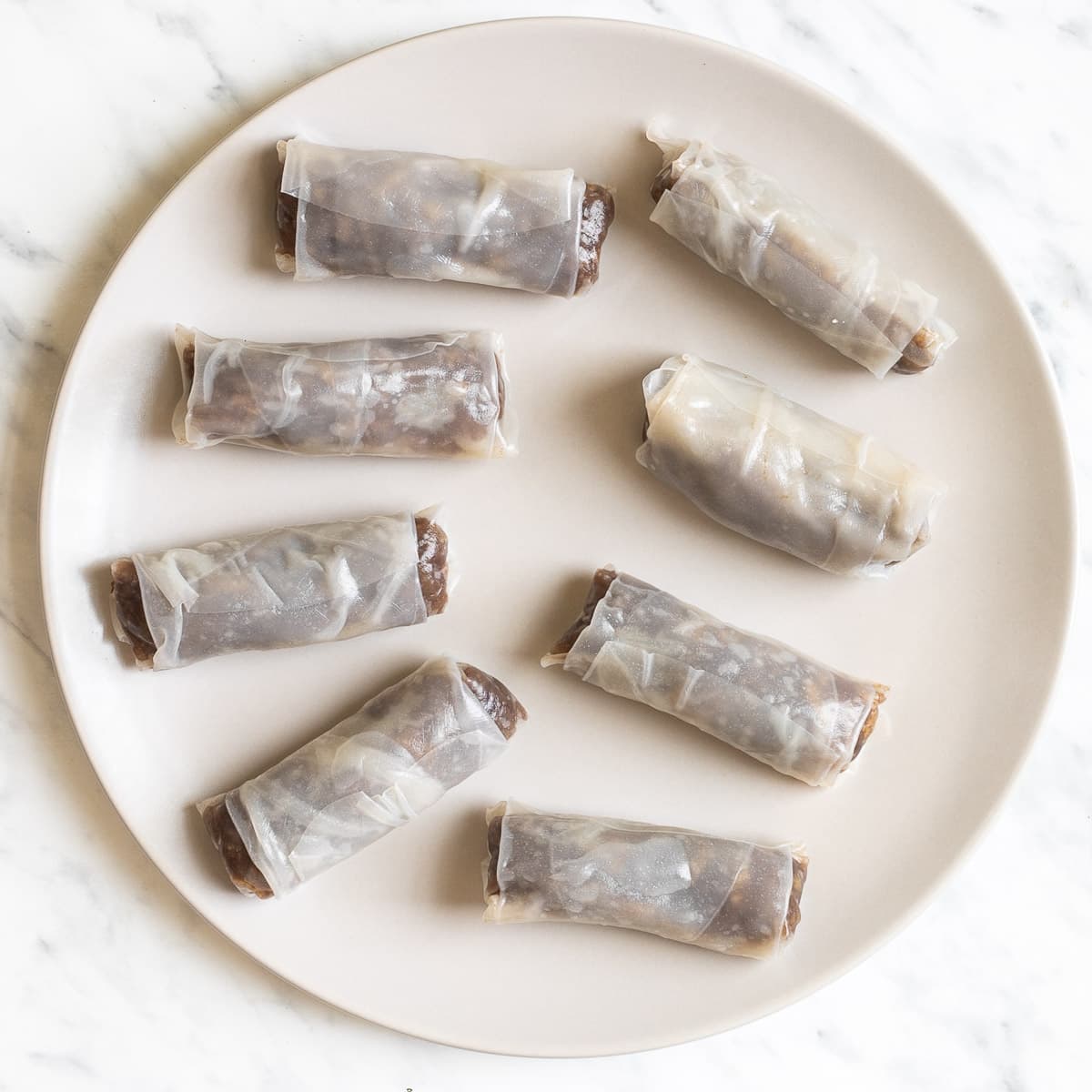 Finished rice paper rolls with a brown filling in a large white plate.