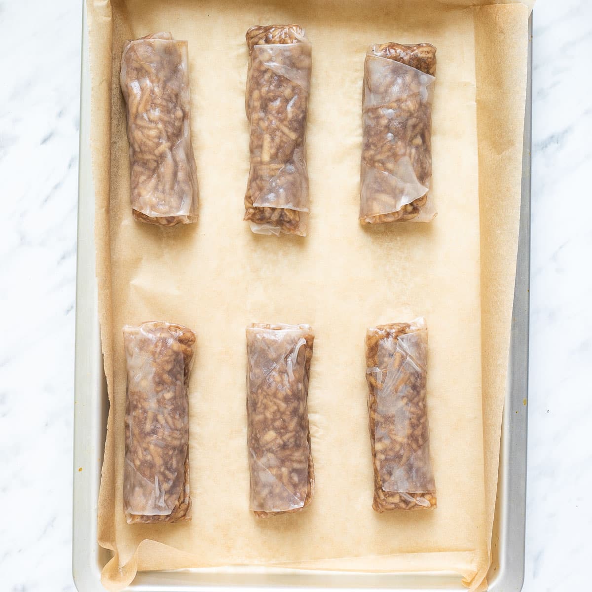 2 rice paper rolls with brown filling in a parchment paper inside a silver baking sheet. 