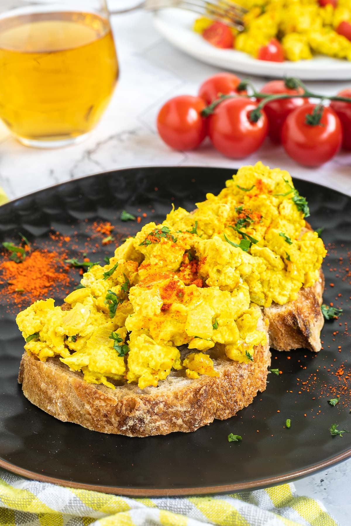 A slice of bread is topped with the yellow tofu crumbles is served on a black plate.