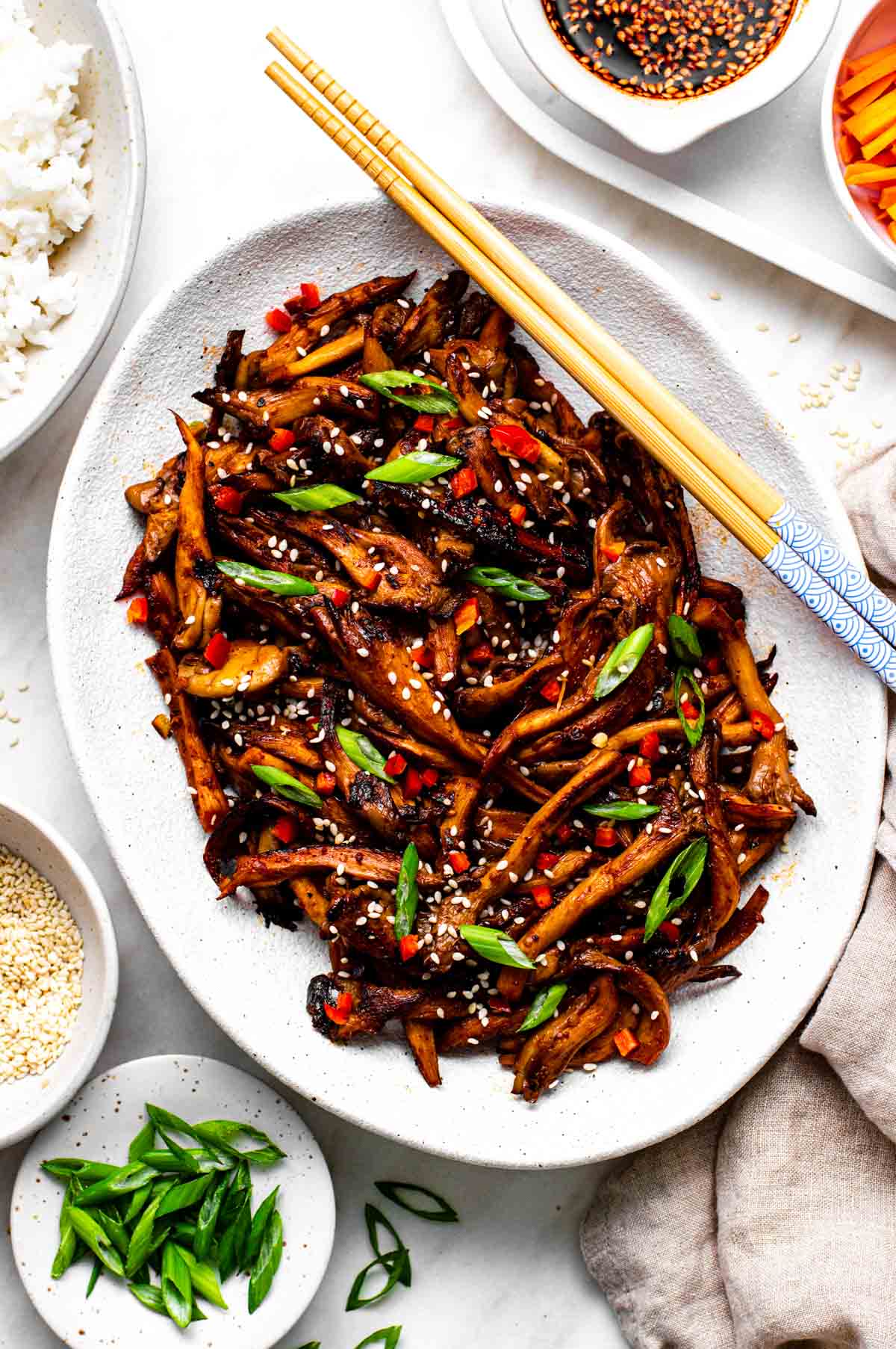 A white plate with stir fried mushrooms and chopsticks.