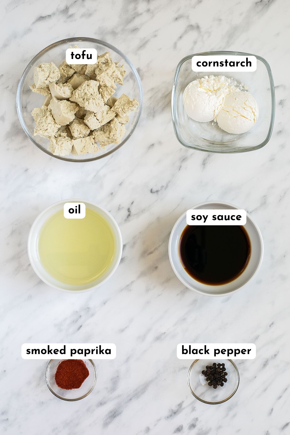 Ingredients of baked tofu in small bowls like tofu pieces, starch, oil, soy sauce, red paprika powder, and black pepper