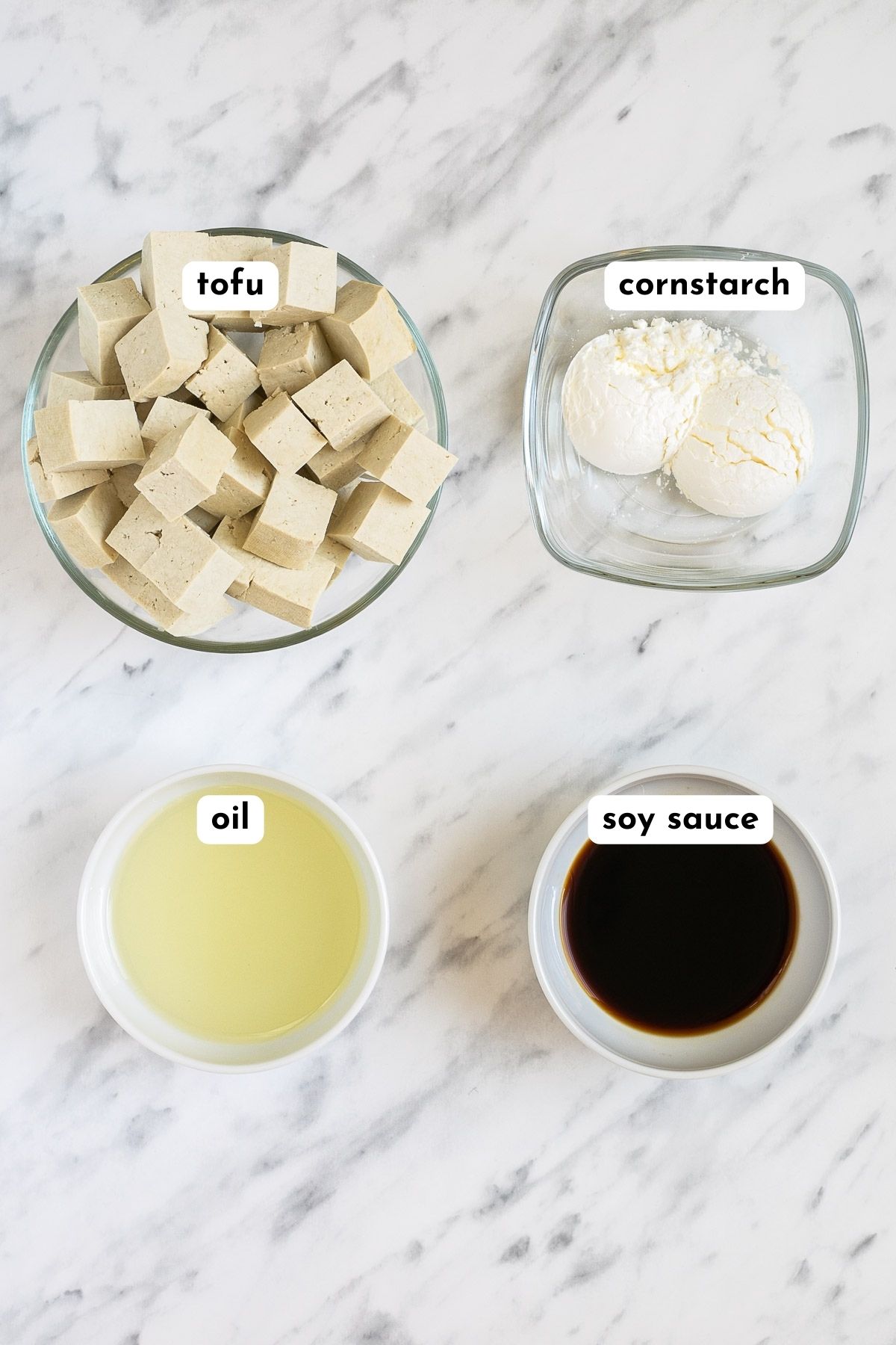 Ingredients of crispy tofu in small bowls like tofu cubes, white powder, oil, and dark soy sauce