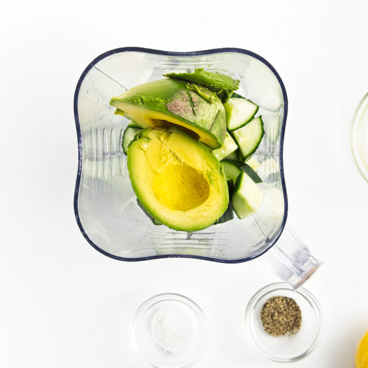 A blender with avocado, chopped cucumber and onion.
