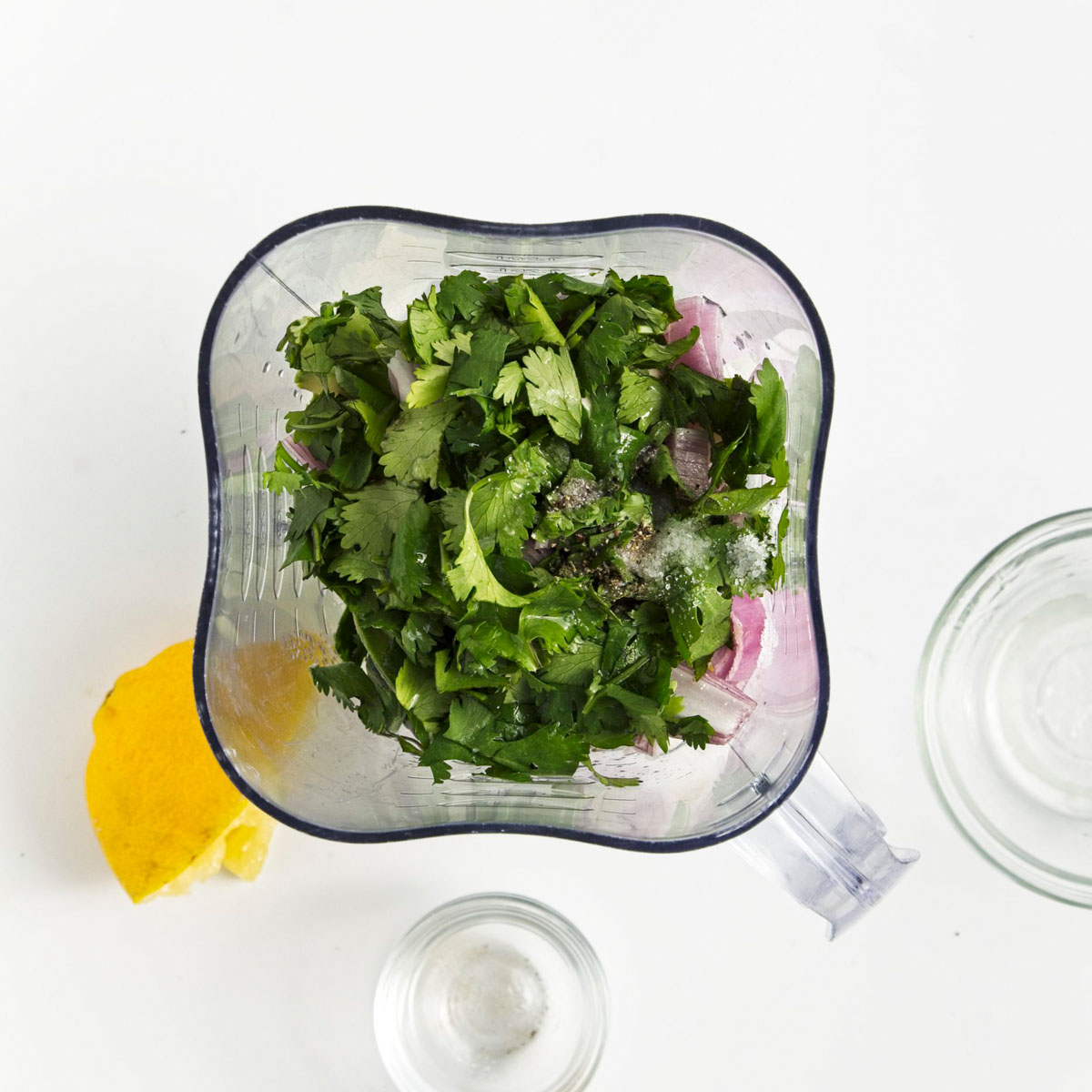 Blender with fresh herbs above chopped veggies.