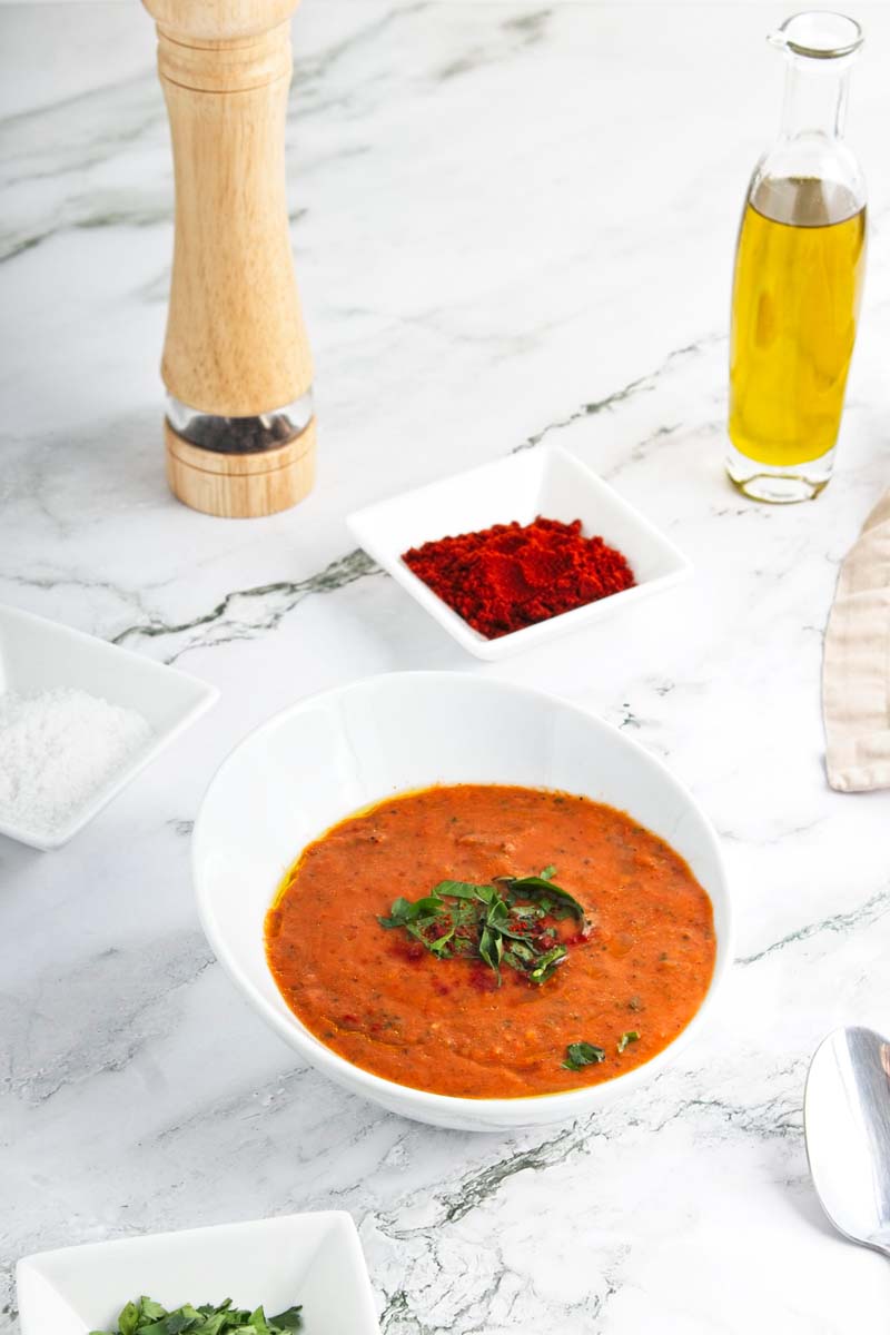 Red soup topped with chopped basil in a white bowl.