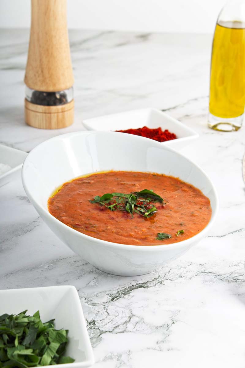 Red soup topped with chopped basil in a white bowl.