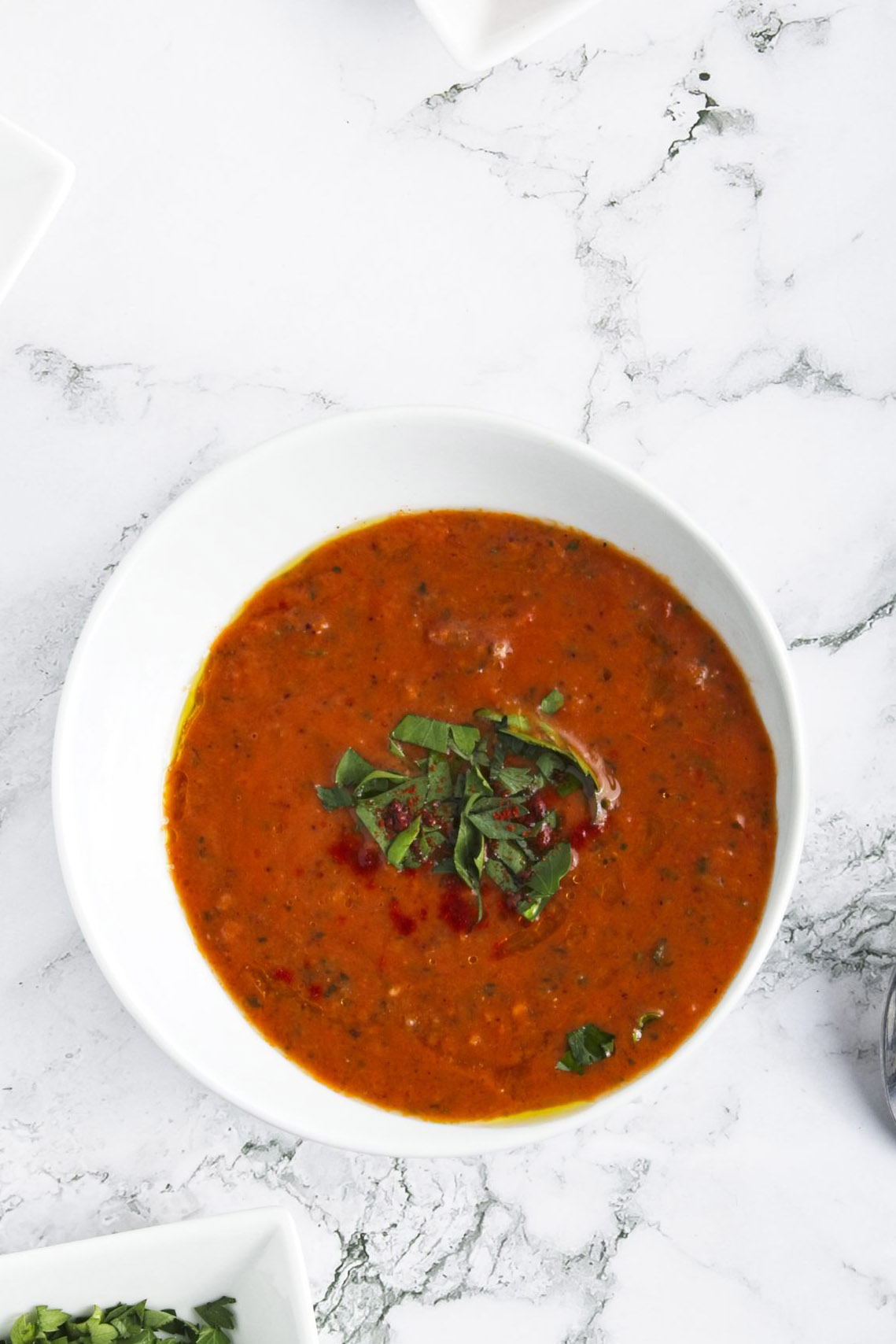Red soup topped with chopped basil in a white bowl.