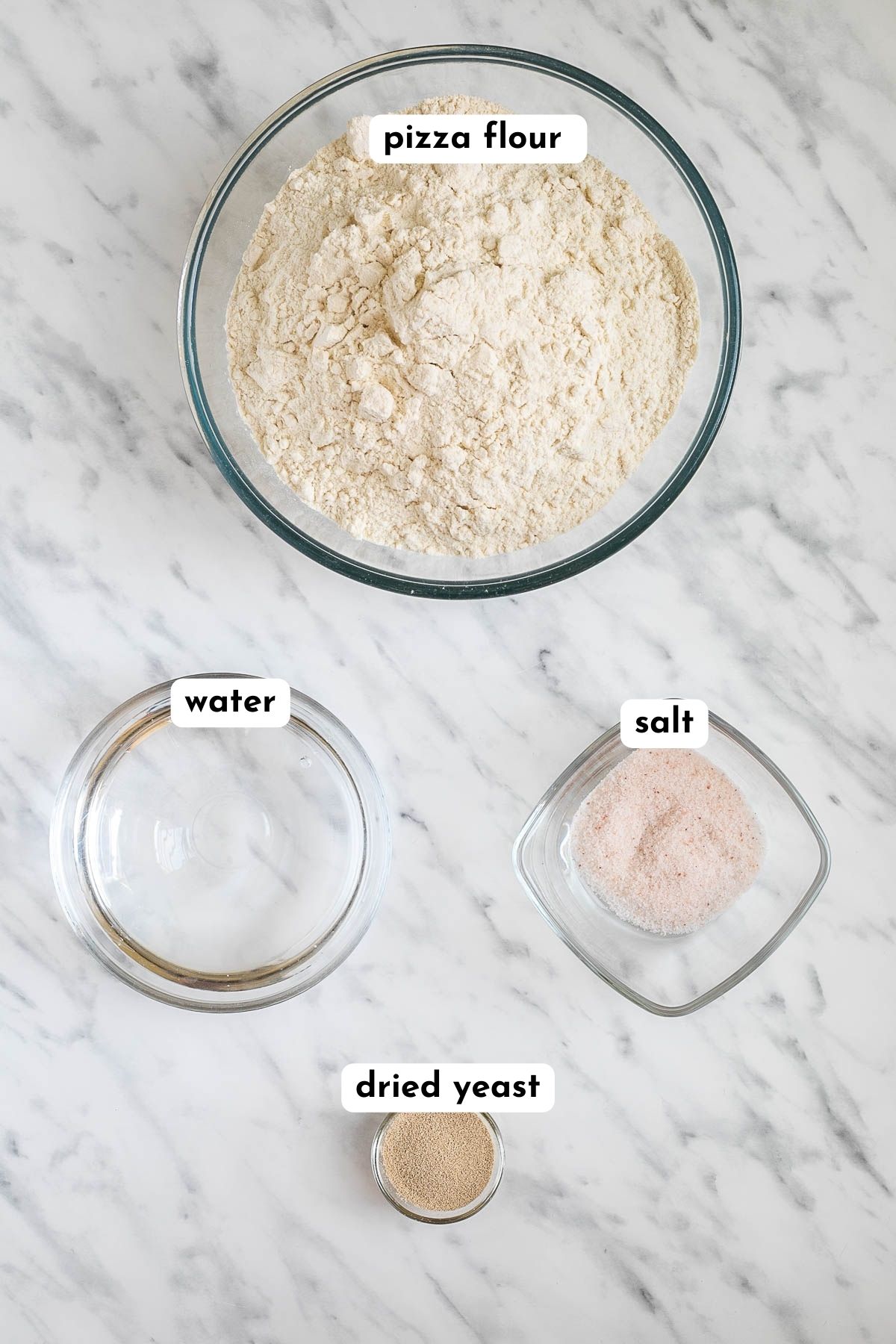 Ingredients of pizza dough in small glass bowls like pizza flour, water, salt, and dry yeast