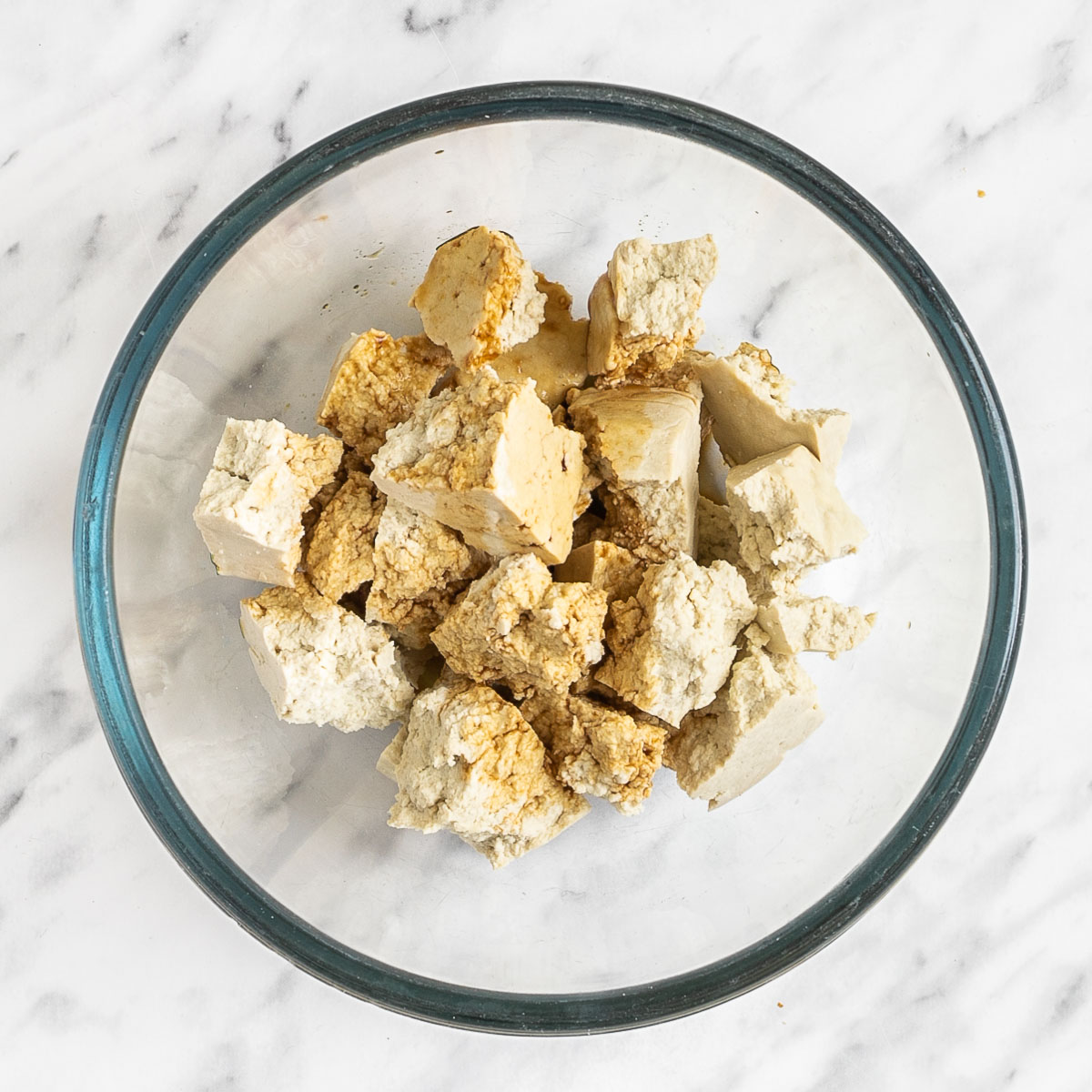 White tofu pieces with soy sauce sprinkled on them in a glass bowl.