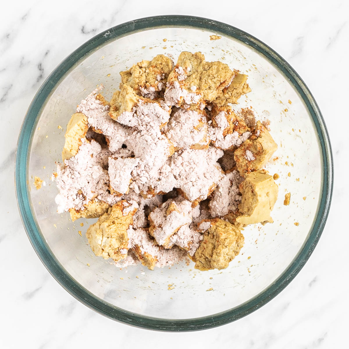 White tofu pieces with spices and corn starch sprinkled on them in a glass bowl.