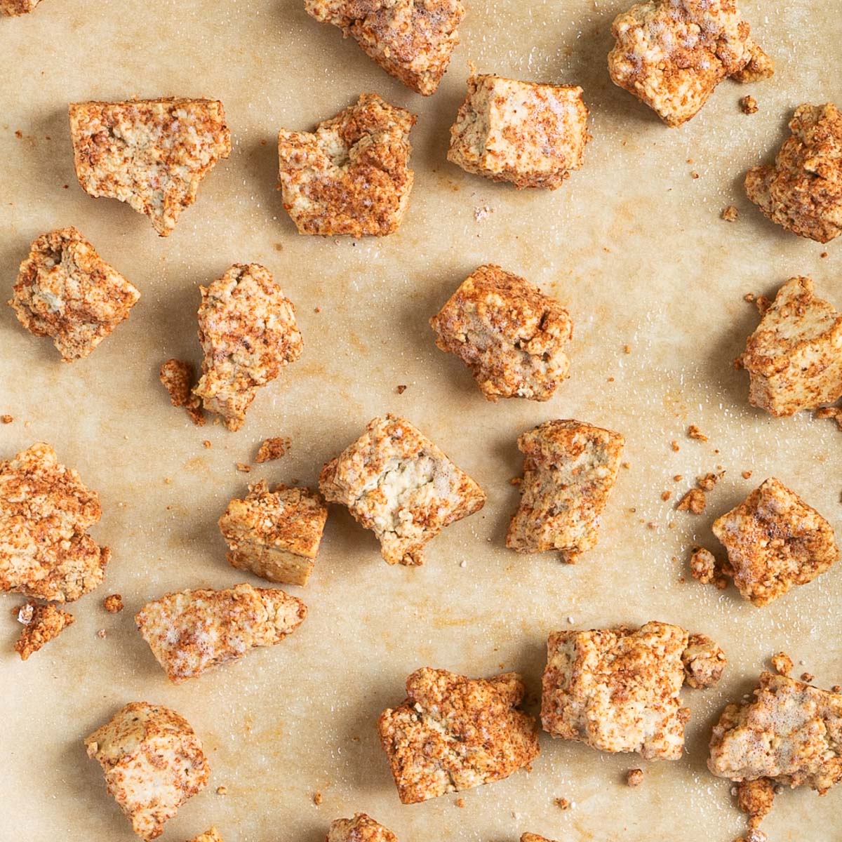Unbaked tofu pieces covered in red white brown spices on a parchment paper.