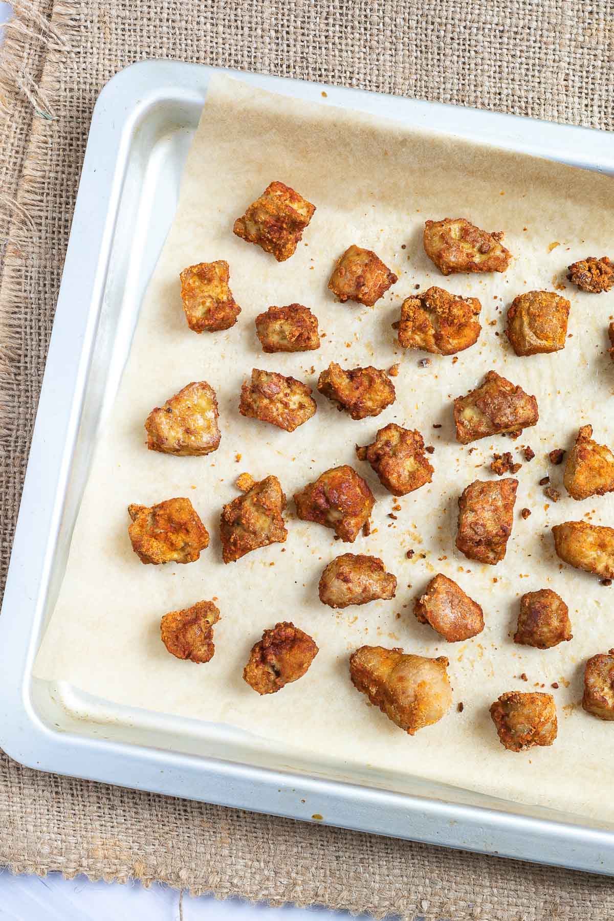 Baked, redish brown tofu pieces on a parchment paper in a silver baking tray.