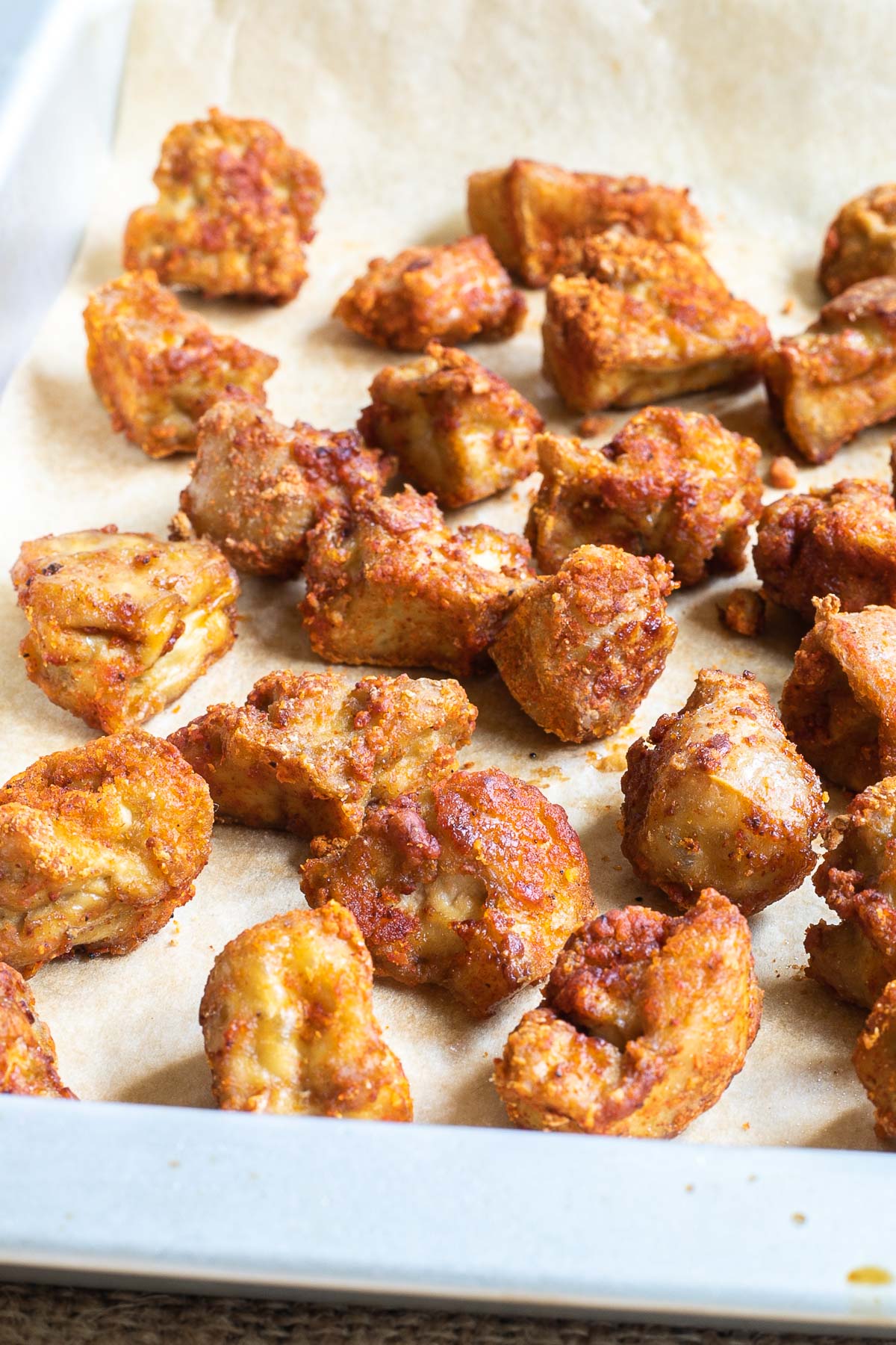 Baked, redish brown tofu pieces on a parchment paper in a silver baking tray.