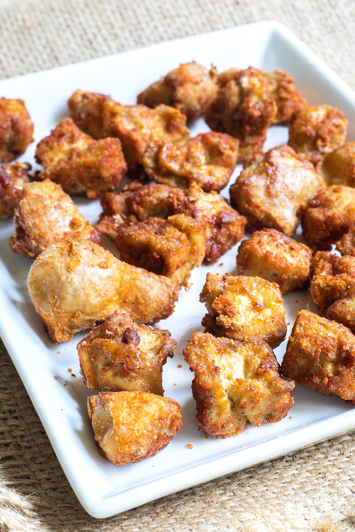 Baked, redish brown tofu pieces on white square plate.