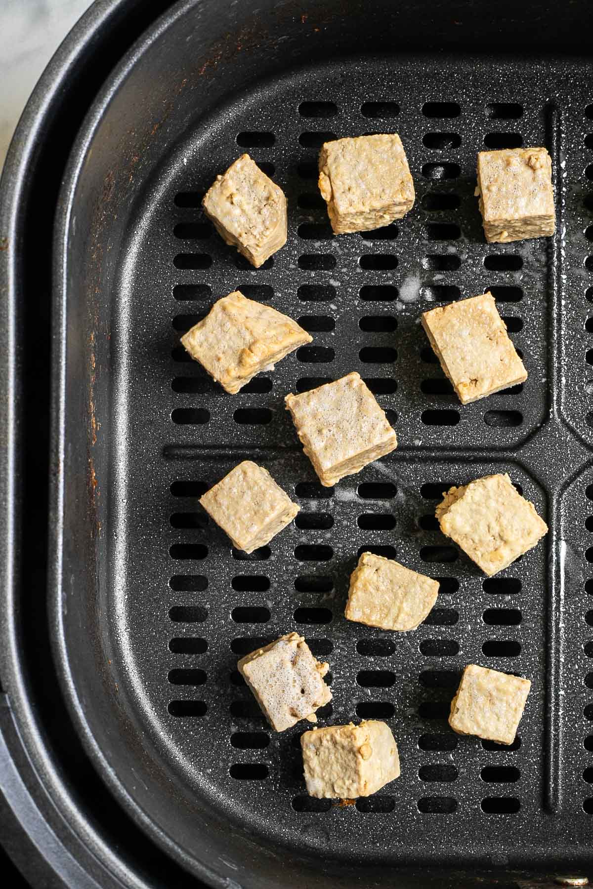 Light brown tofu cubes in an air fryer basket