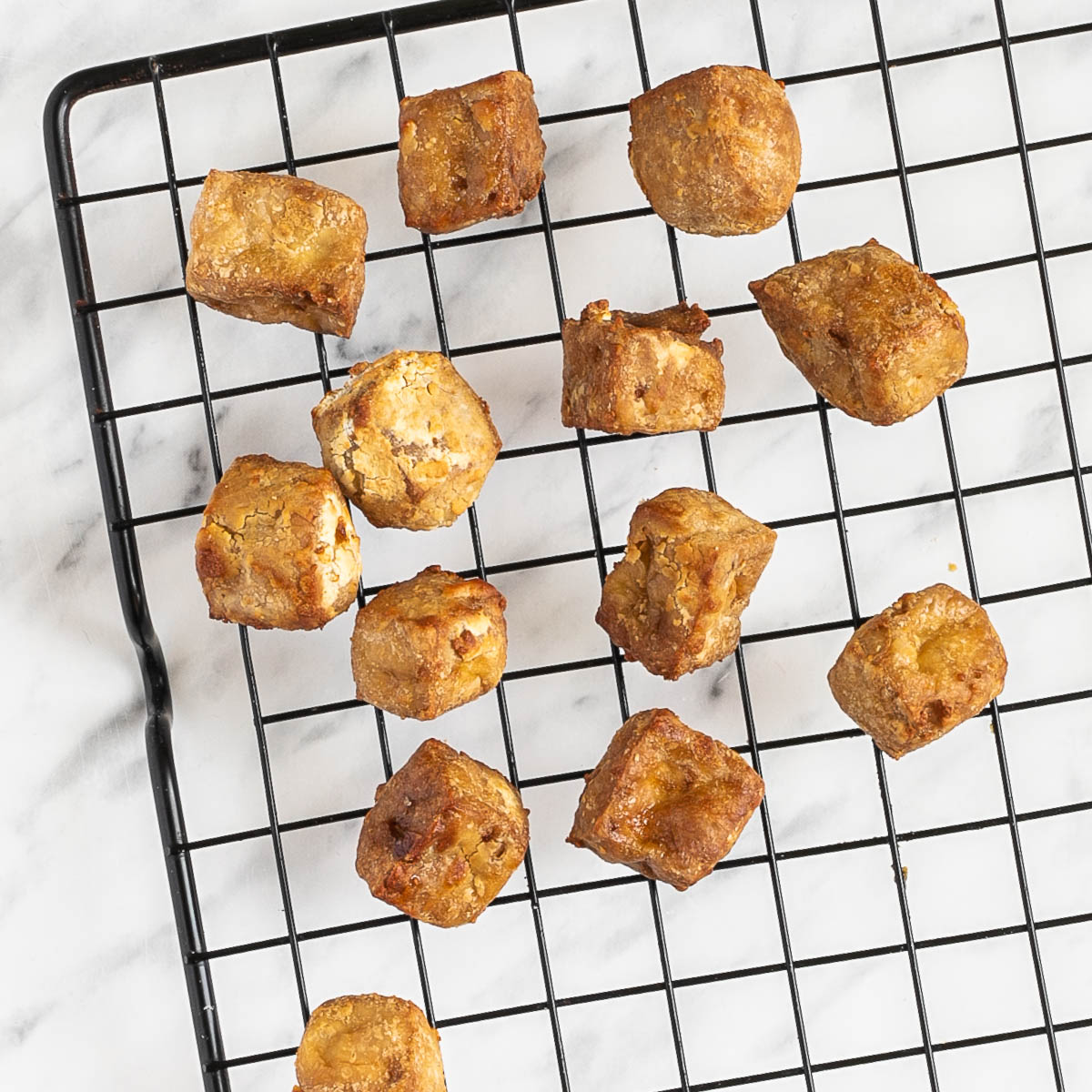 Crispy golden brown tofu cubes on a black wire rack.
