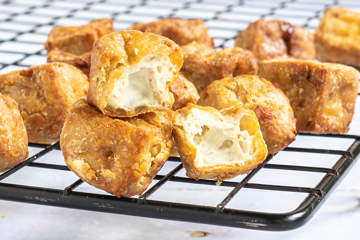 Crispy golden brown tofu cubes stacked on a black wire rack. 2 of them is cut in half to see the spongy inside.