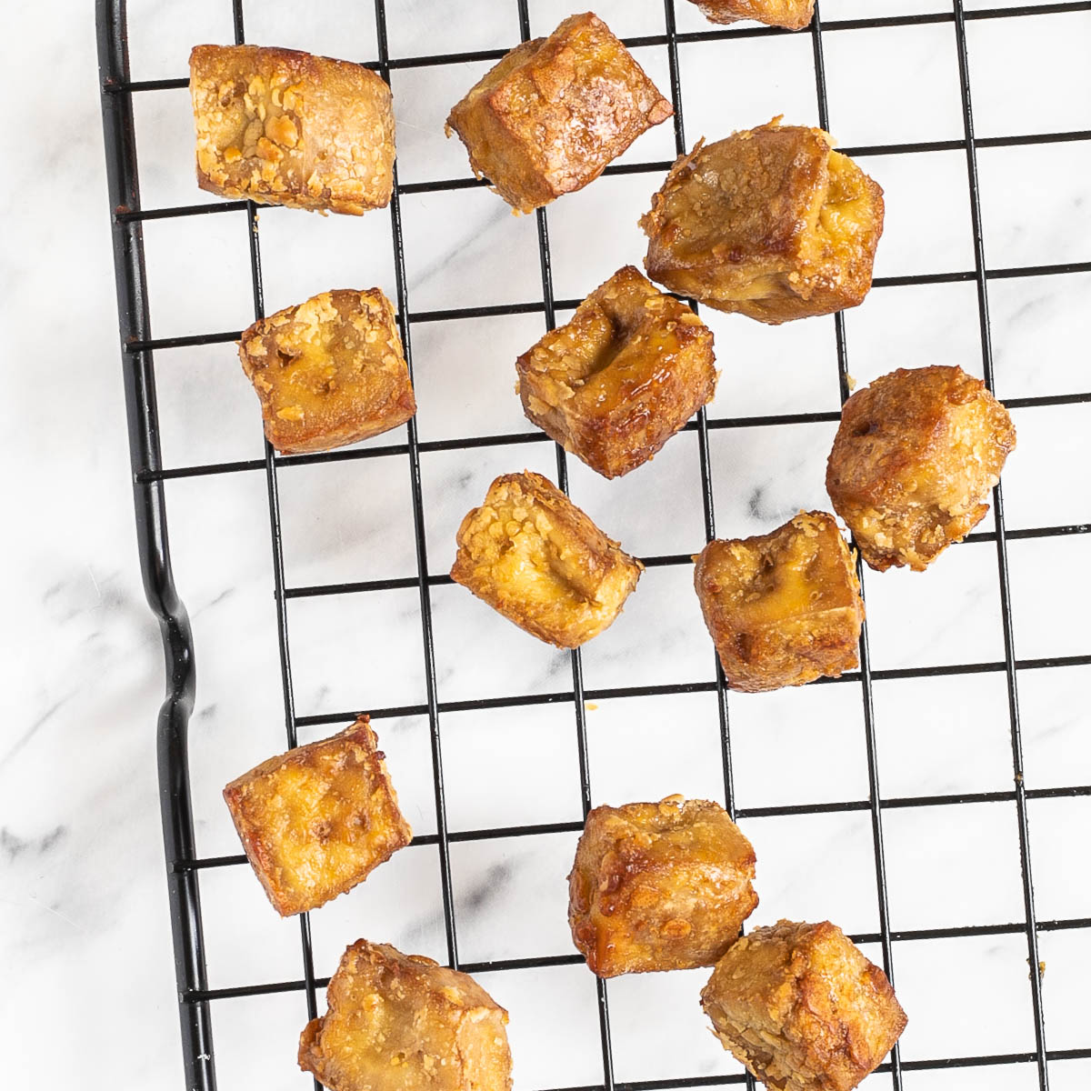 Crispy golden brown tofu cubes on a black wire rack.