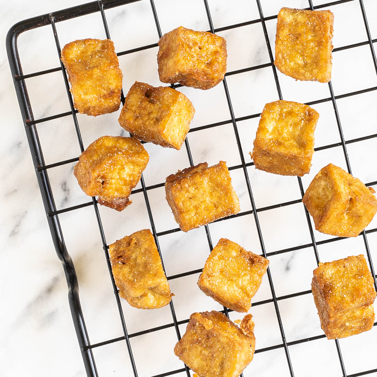 Crispy golden brown tofu cubes on a black wire rack.