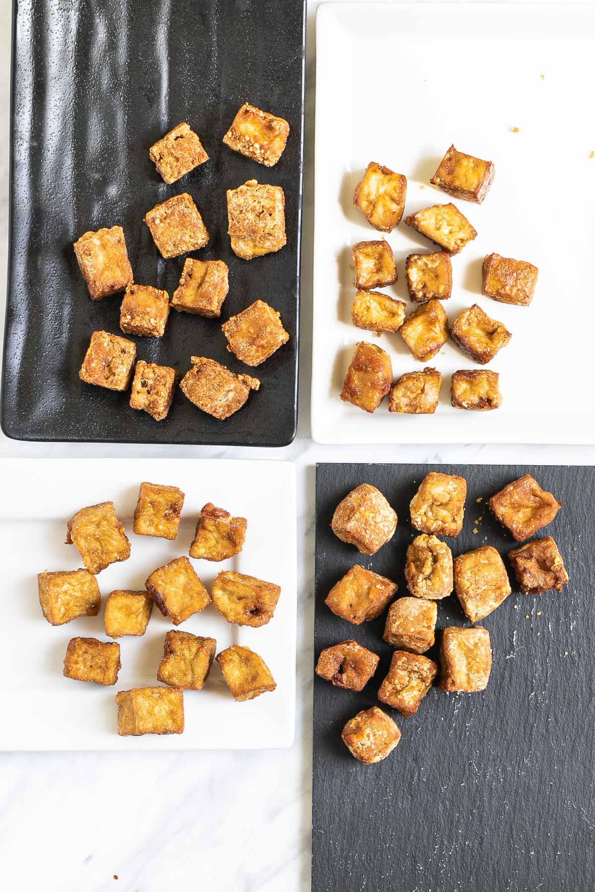 Crispy brown tofu cubes on 4 different plates of white and black.