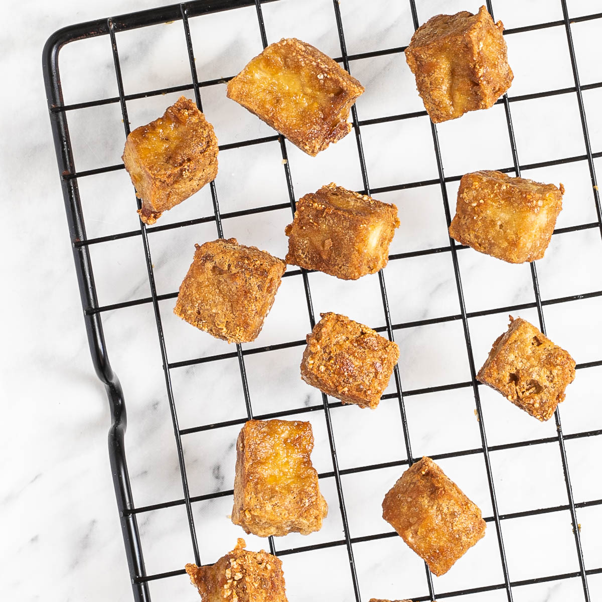 Crispy golden brown tofu cubes on a black wire rack.